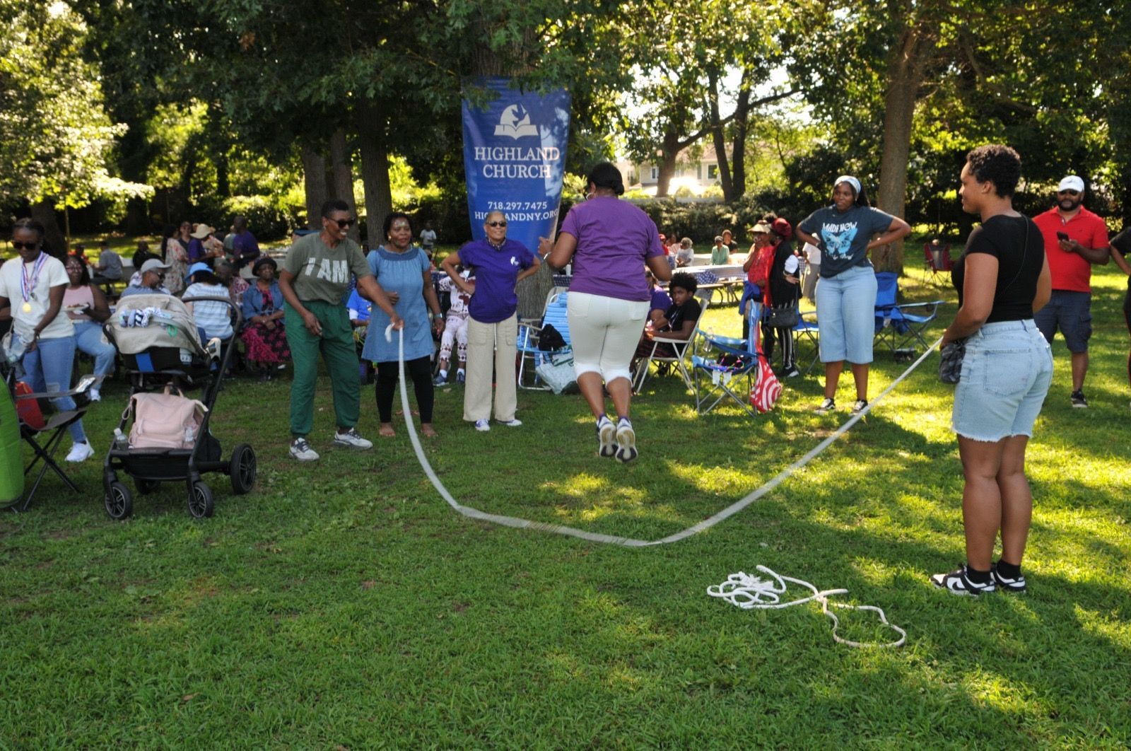 People gathered on a grassy field watching a rope-tug game near a blue banner.