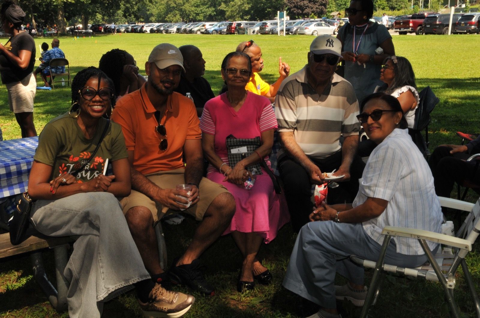 Group of people seated on folding chairs in a sunny park, smiling and posing together