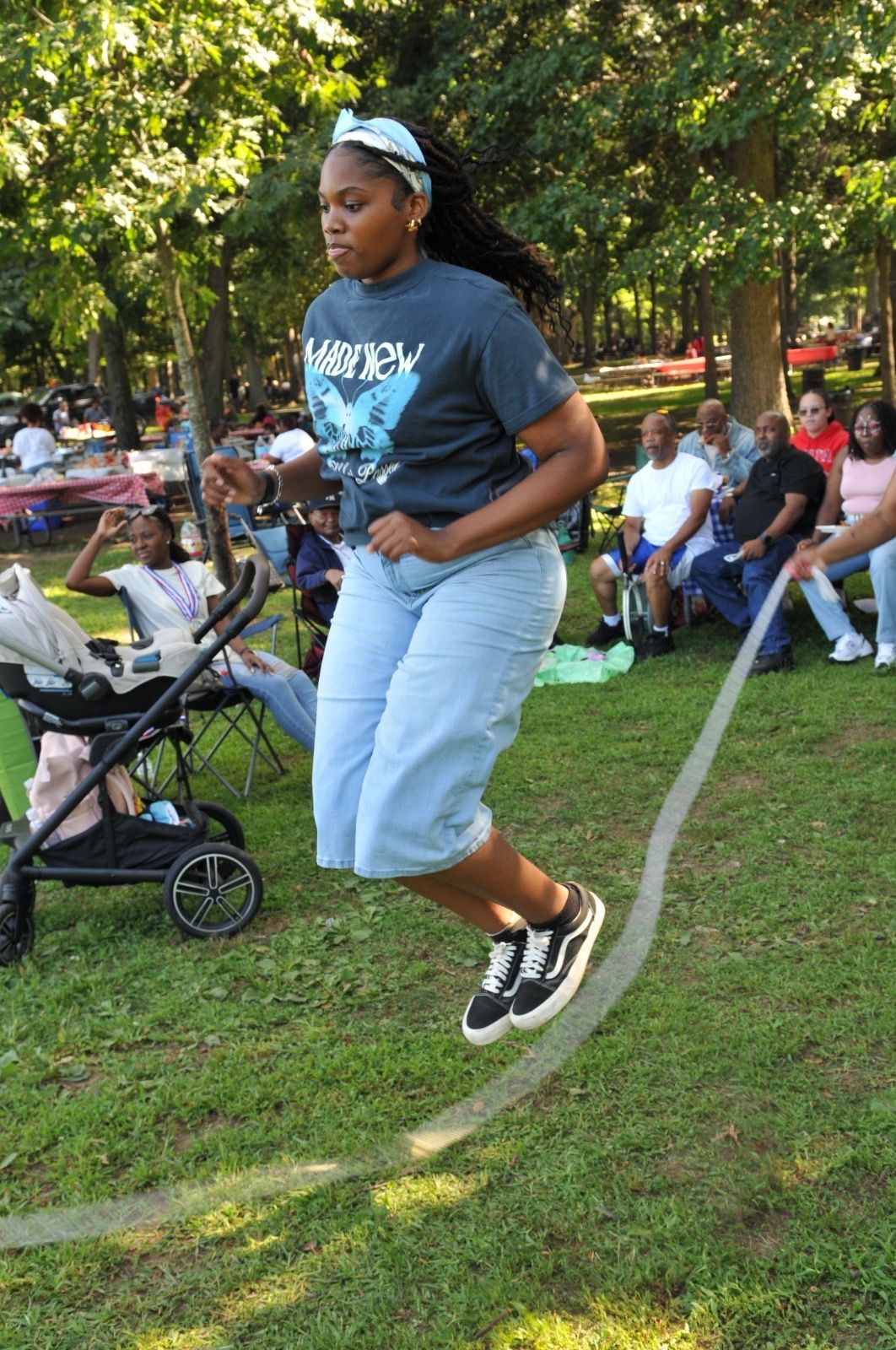 Woman jumping rope in a park, wearing a gray shirt, light jeans, and black sneakers.