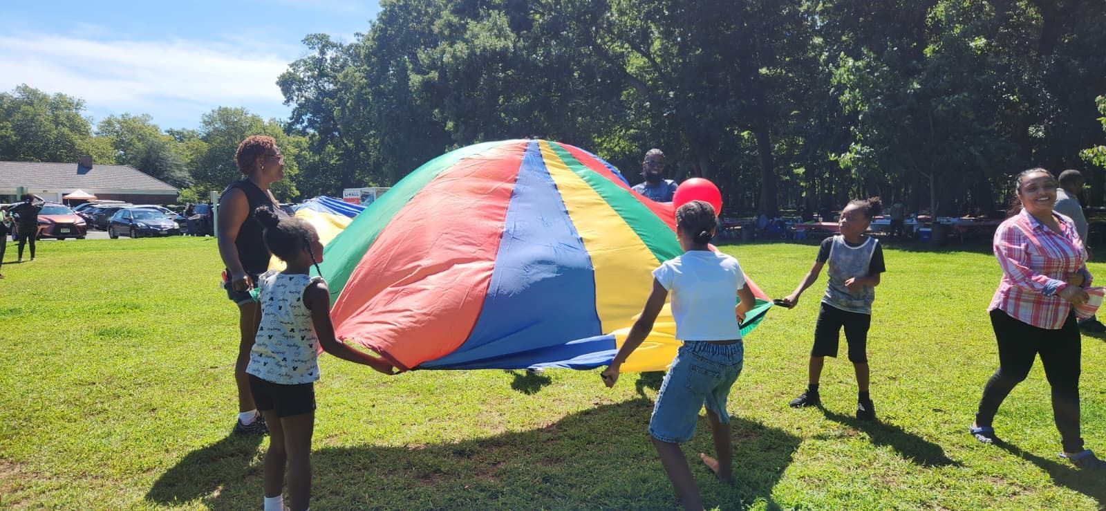 Children play with a colorful parachute on a sunny grassy field.