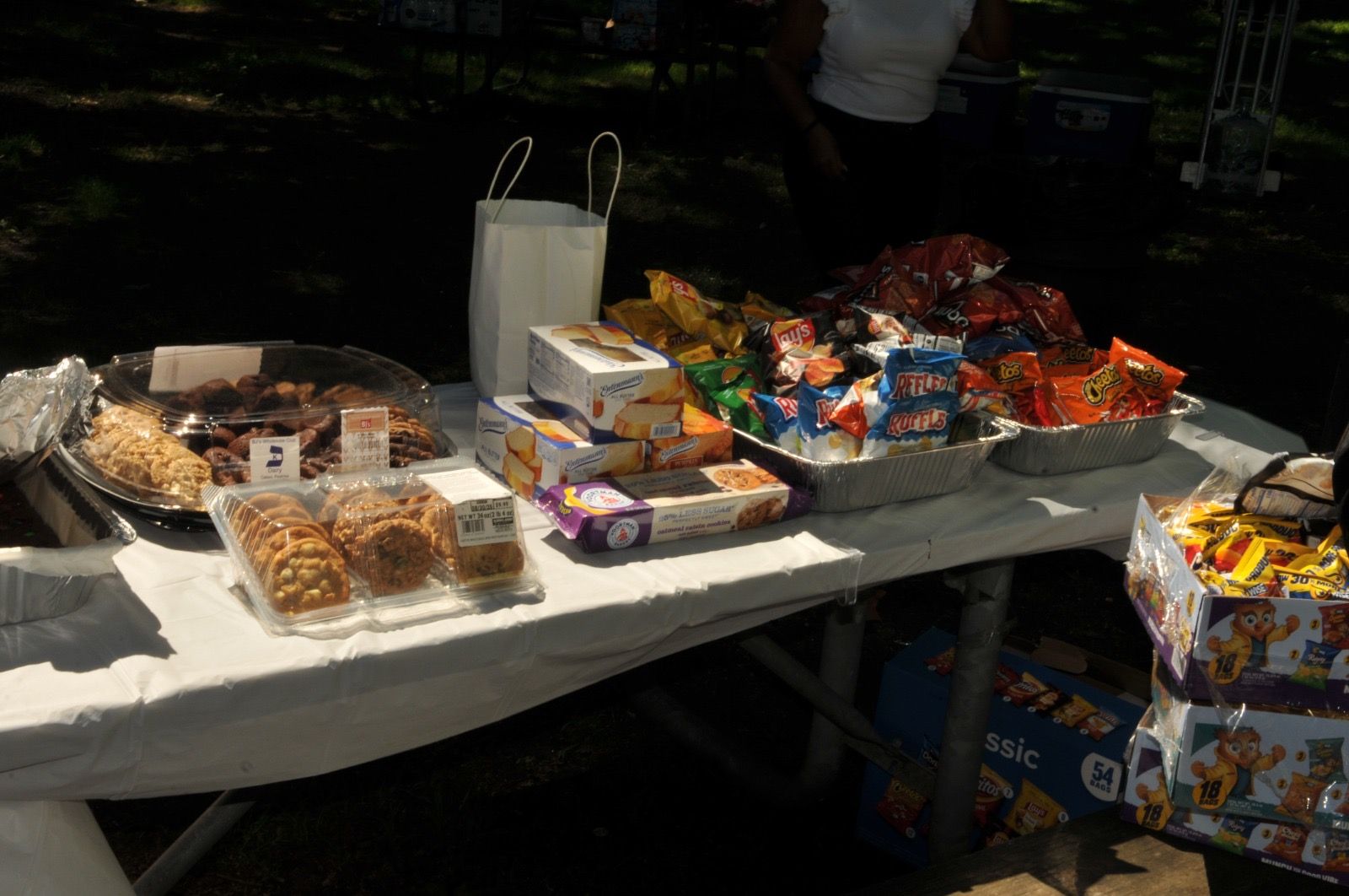 Table of assorted snacks and candies at an outdoor market stall under shade