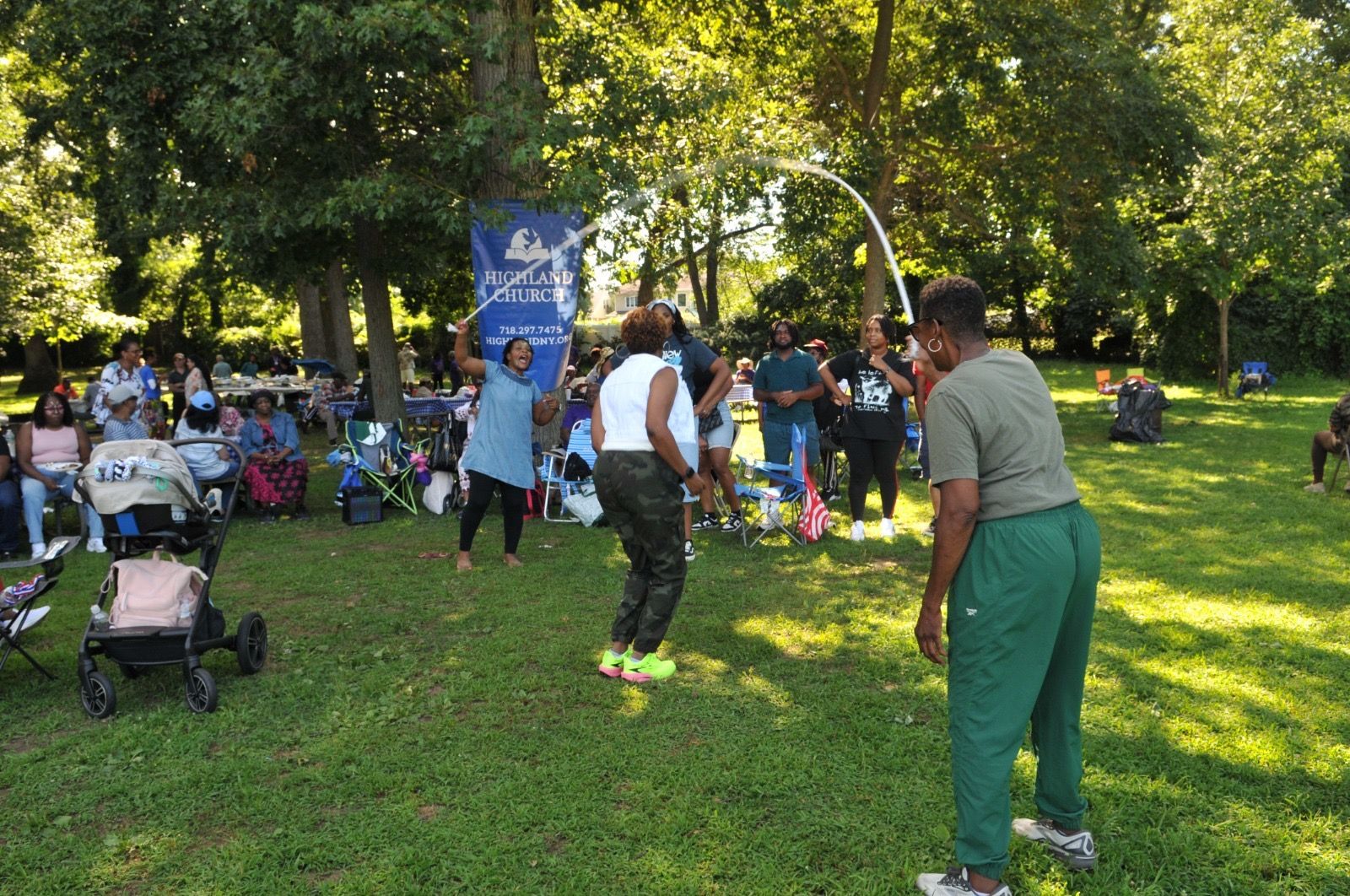 People gathered in a sunny park, chatting and dancing on the grass near a stroller.