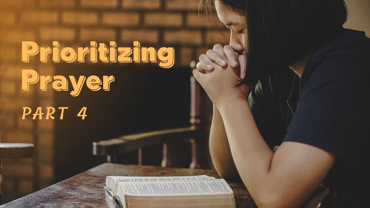 A woman is praying while sitting at a table with a bible.