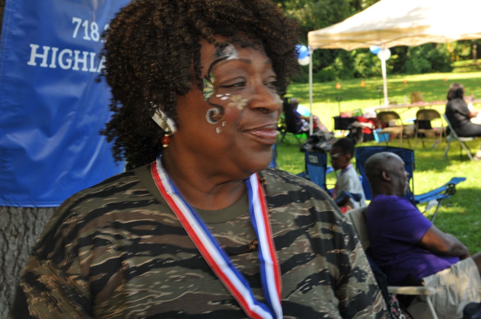 Woman wearing a medal at an outdoor event, smiling in front of a blue banner and tents.