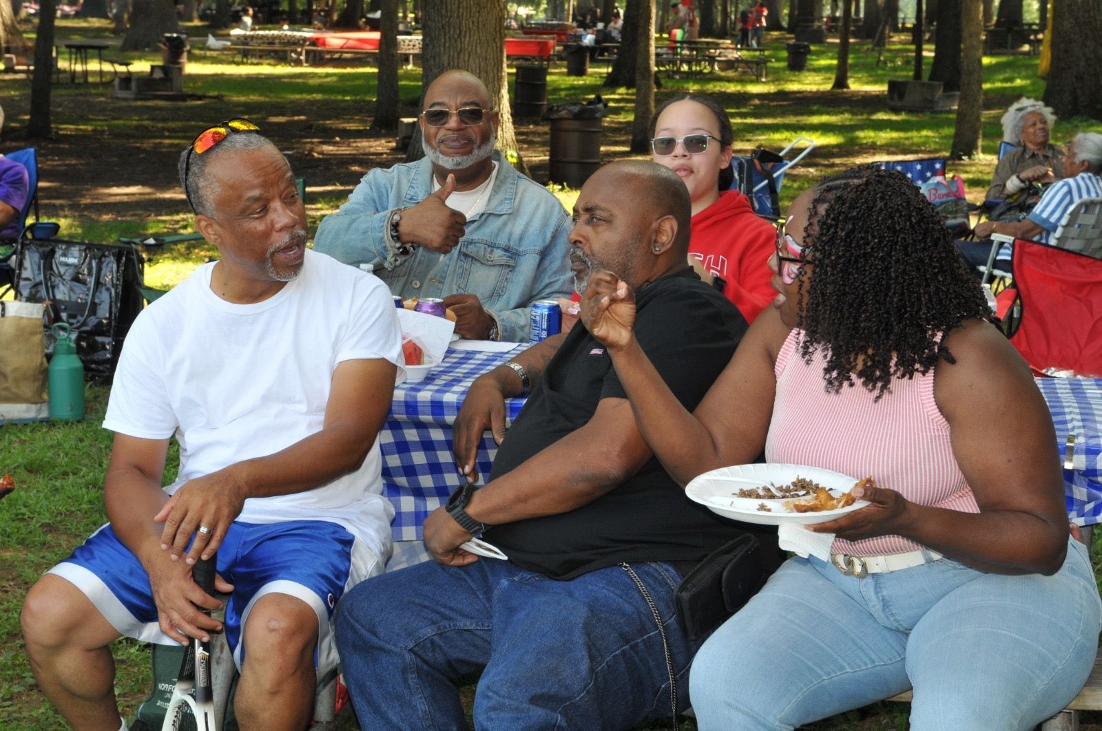 Friends sitting and chatting at a picnic table in a park, with plates of food and drinks.