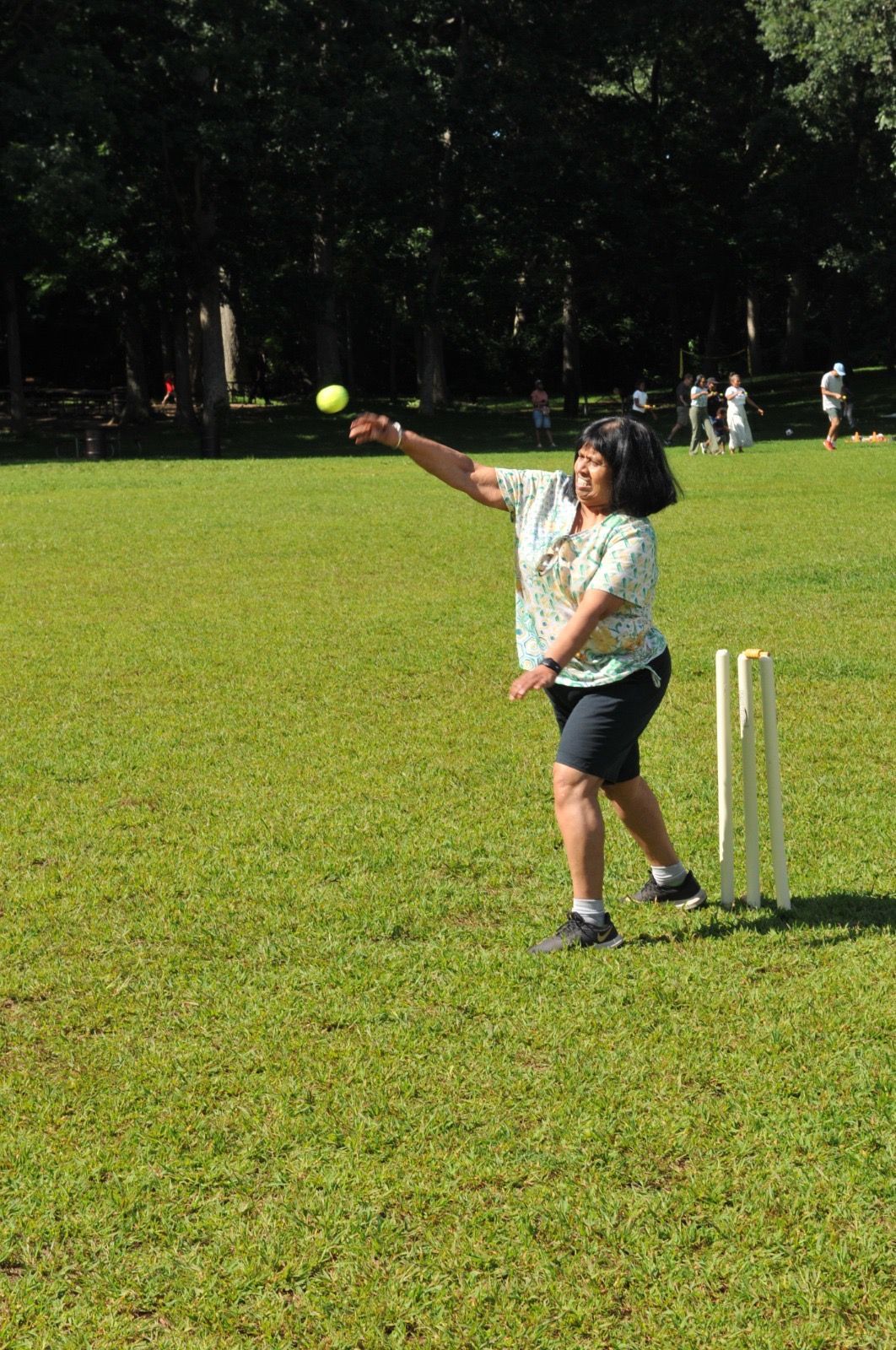 Person in a grassy field throwing a ball near wickets during a game of cricket