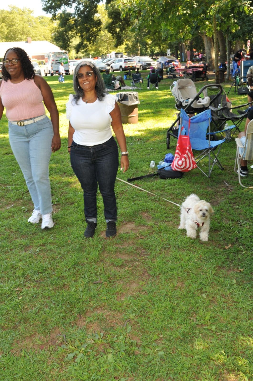 Two people standing on grass in a park with a small white dog nearby and bicycles in the background