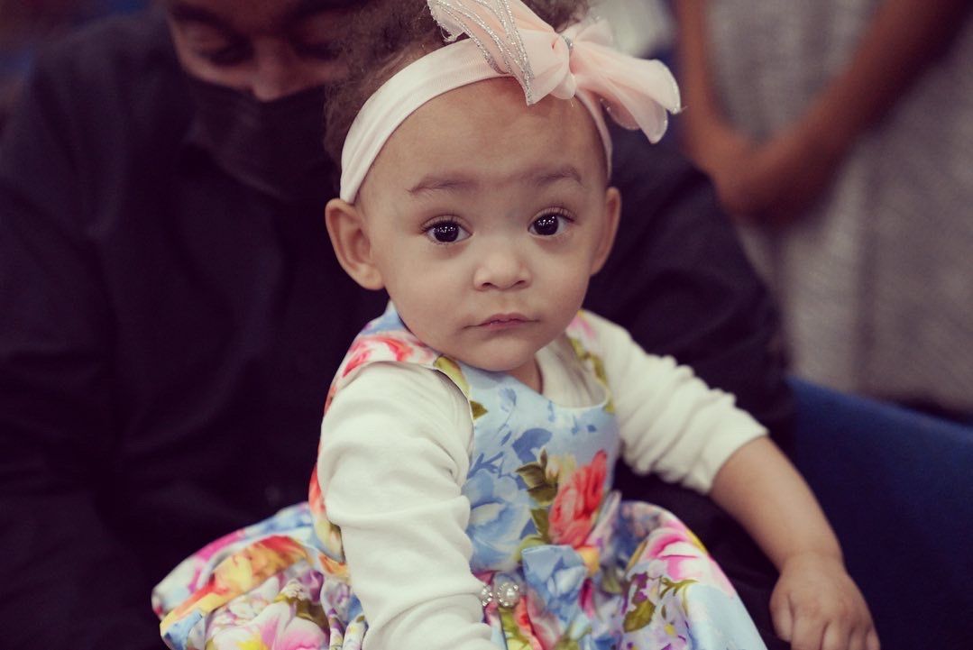 A baby girl wearing a floral dress and headband is sitting next to a man.