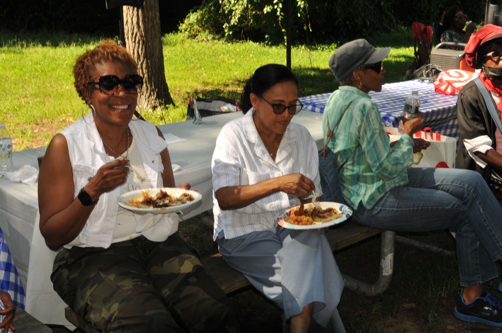 People eating lunch at a picnic table outdoors in a sunny park