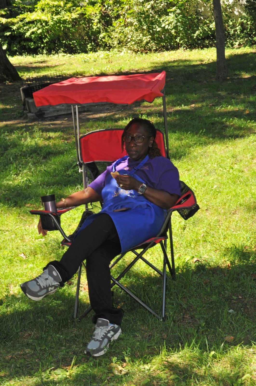 Person seated in a red-and-blue lawn chair on a sunny grassy lawn, holding a cup