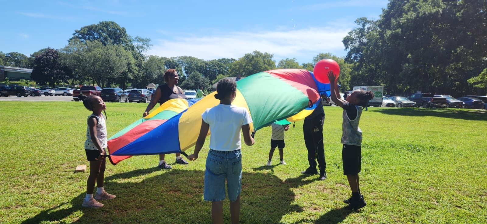People holding a large rainbow parachute on a sunny grassy field