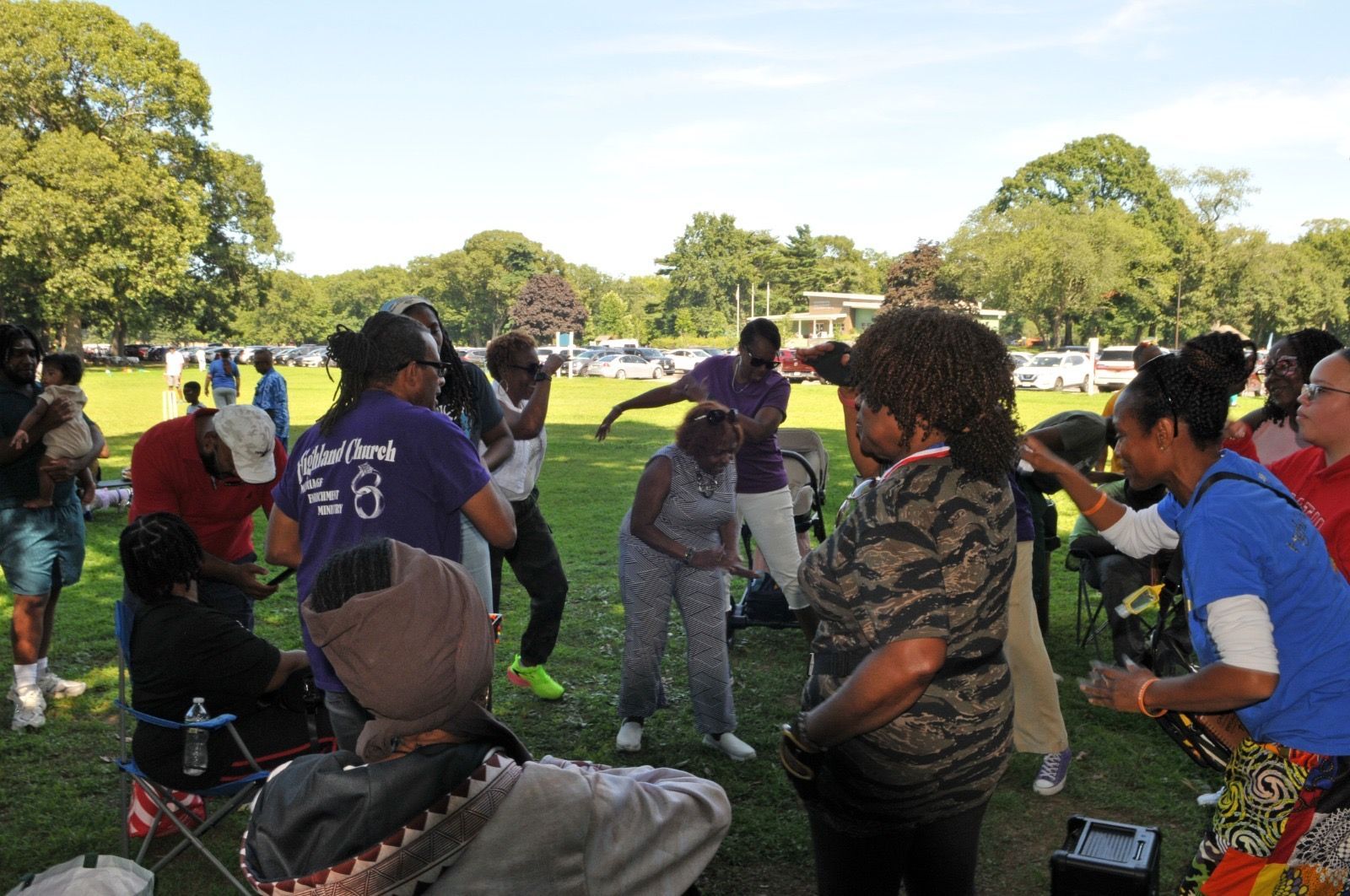 People standing in a grassy park, talking in a loose circle during an outdoor gathering.