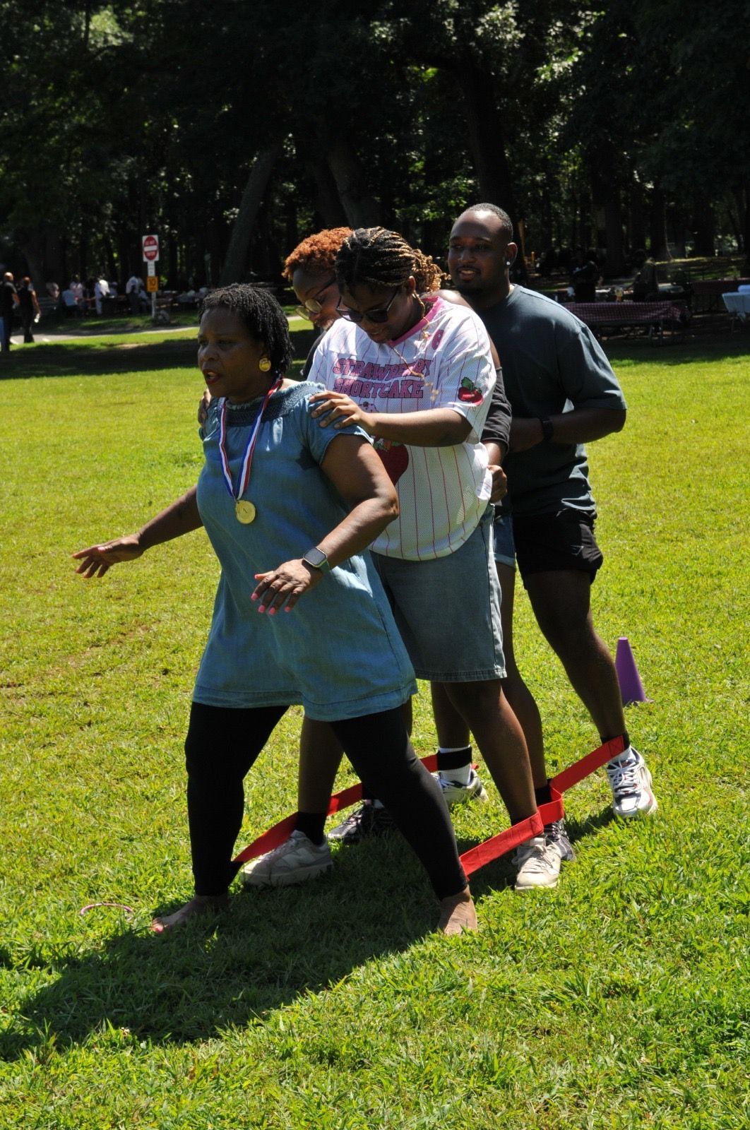 Three people standing together in a grassy park, balancing on red skis with ropes attached.