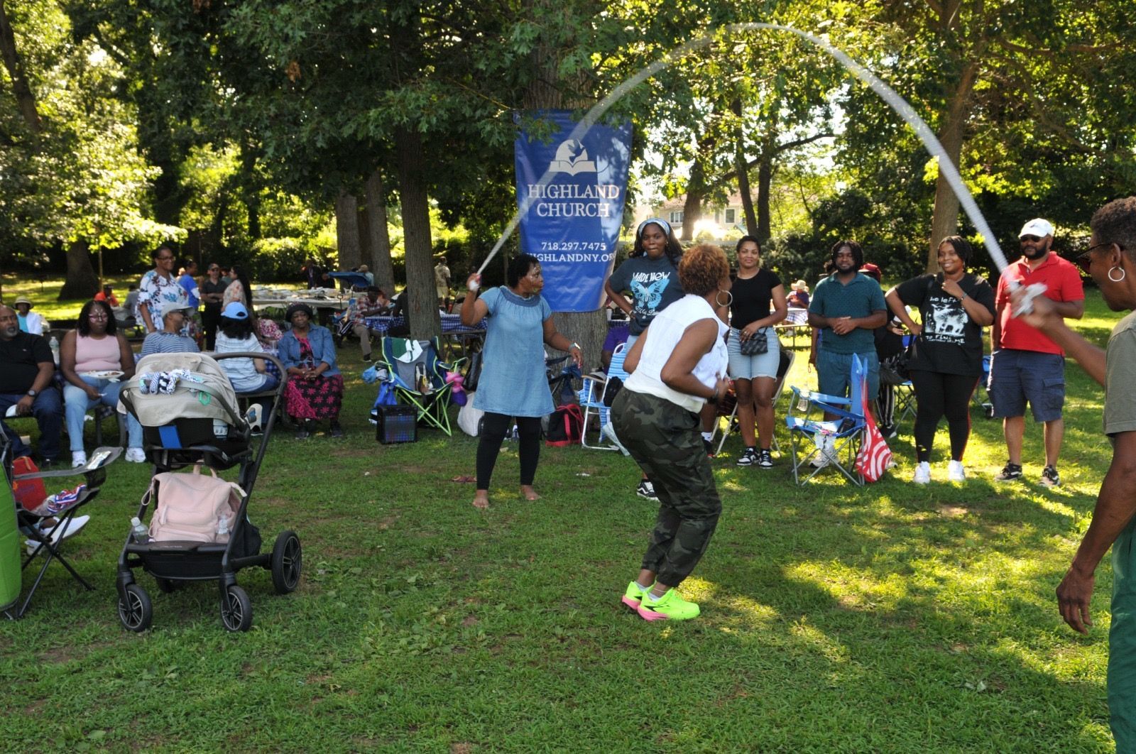 People dancing at a sunny outdoor park gathering with spectators and a stroller nearby