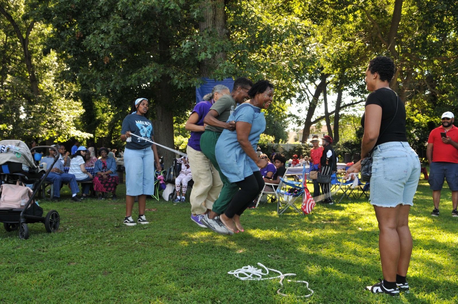 People with sacks racing in a grassy park while others watch nearby