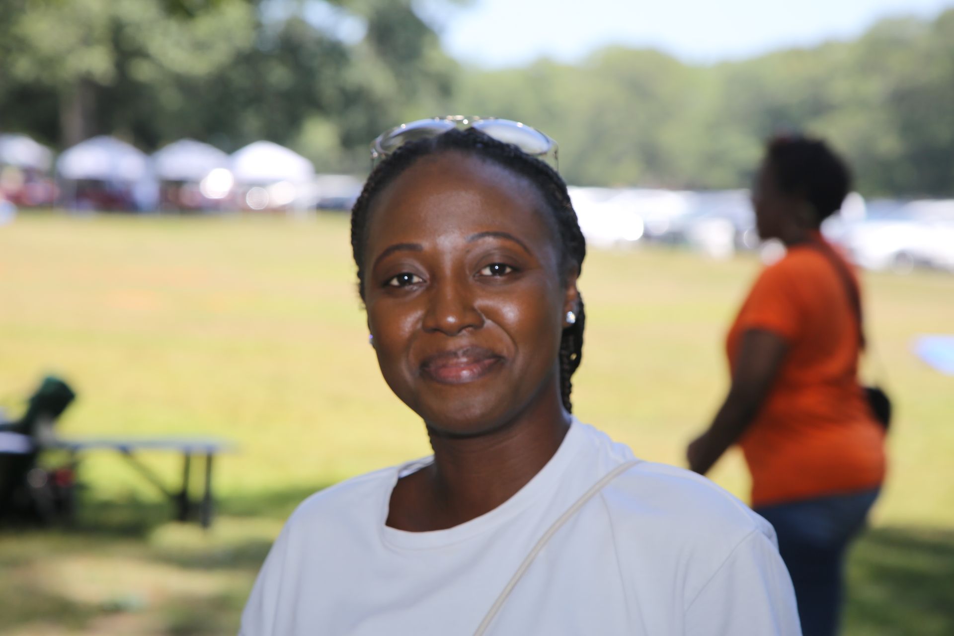 Woman smiling at outdoor event with grassy field and blurred tents in the background. Hempstead Park 2025