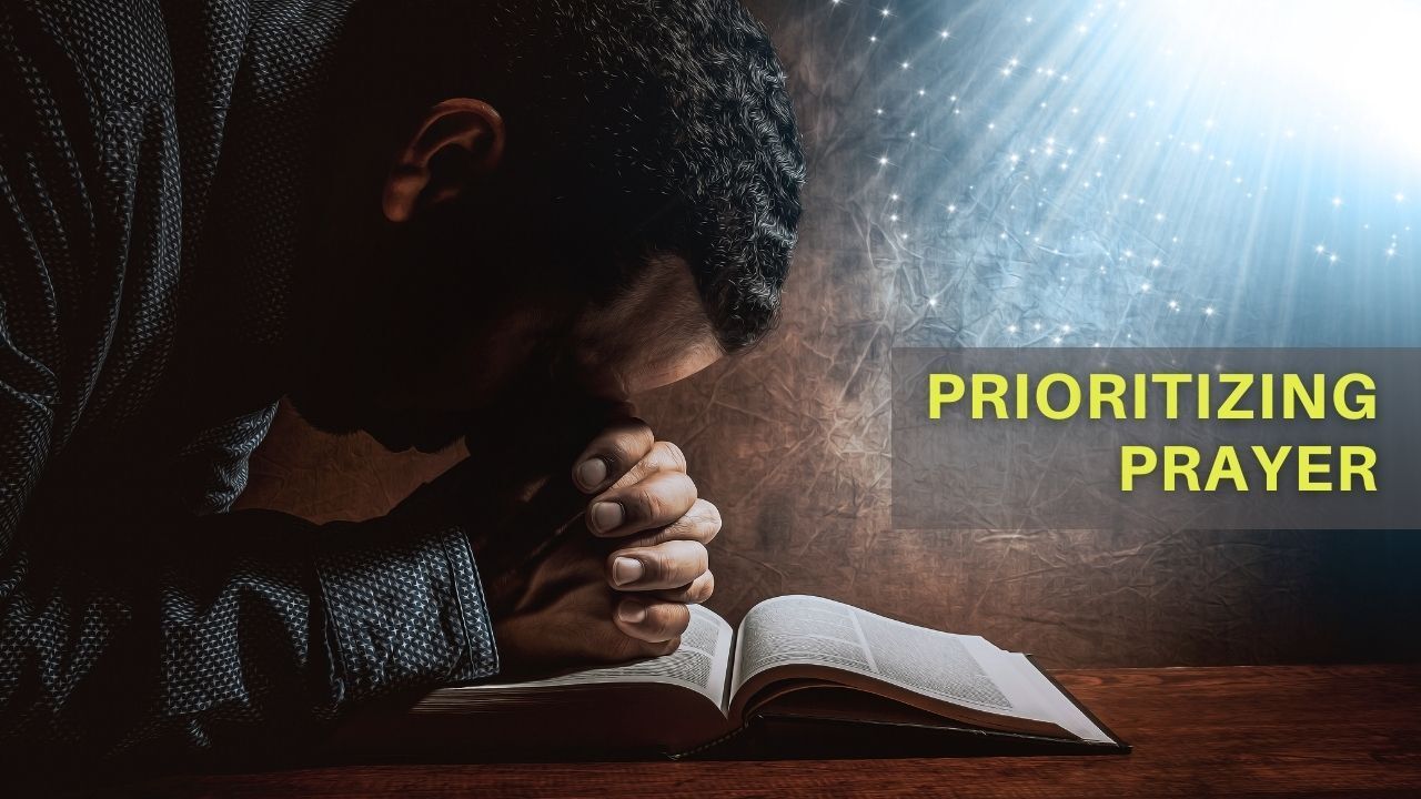 A man is praying over a bible while sitting at a table.