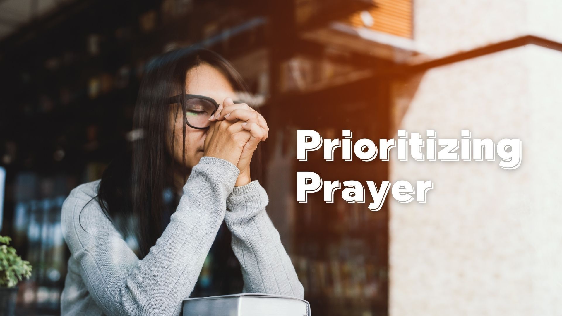 A woman wearing glasses is praying in front of a window.