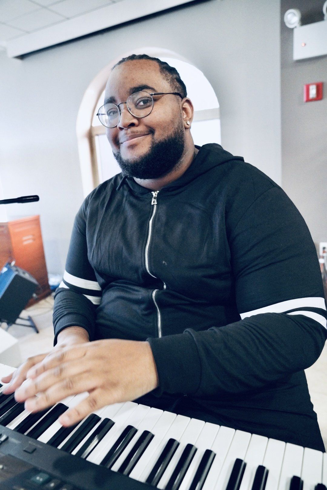 A man with glasses is playing a keyboard and smiling.