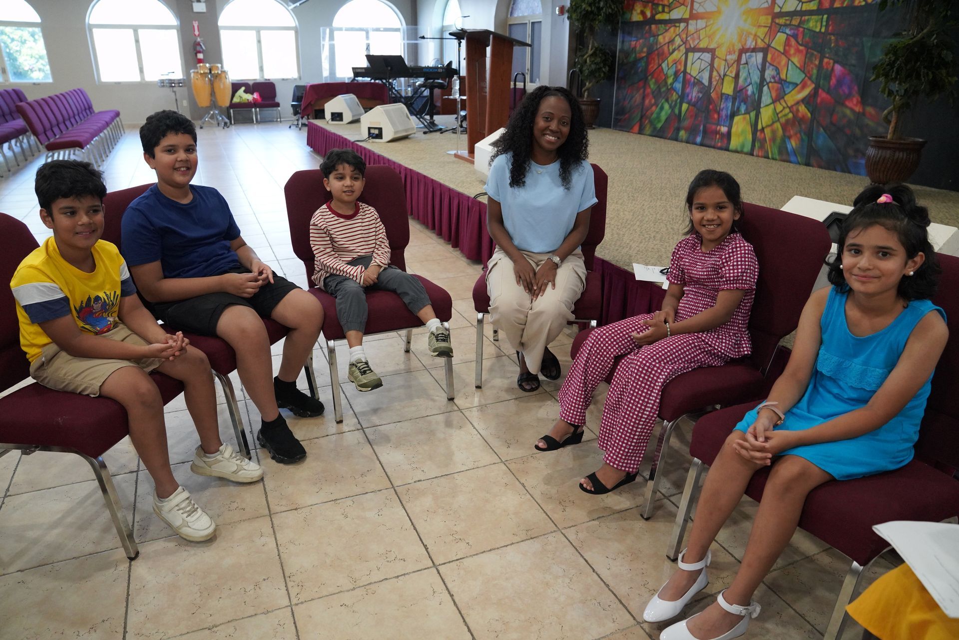 People seated in a circle in a bright room with tiled floors and colorful wall art.