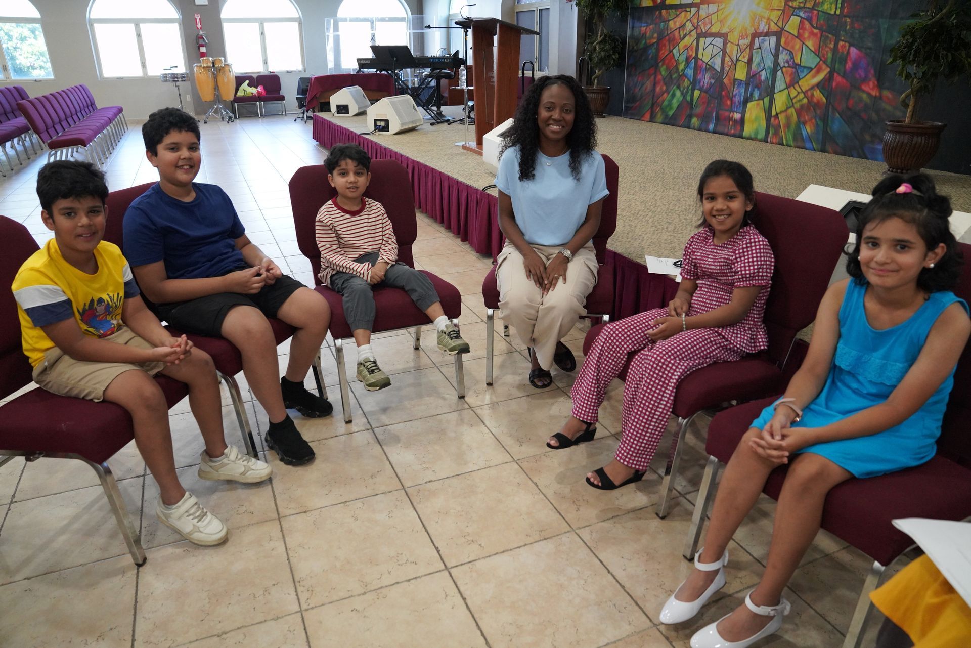 Children seated in a circle in a bright room with colorful artwork on the walls