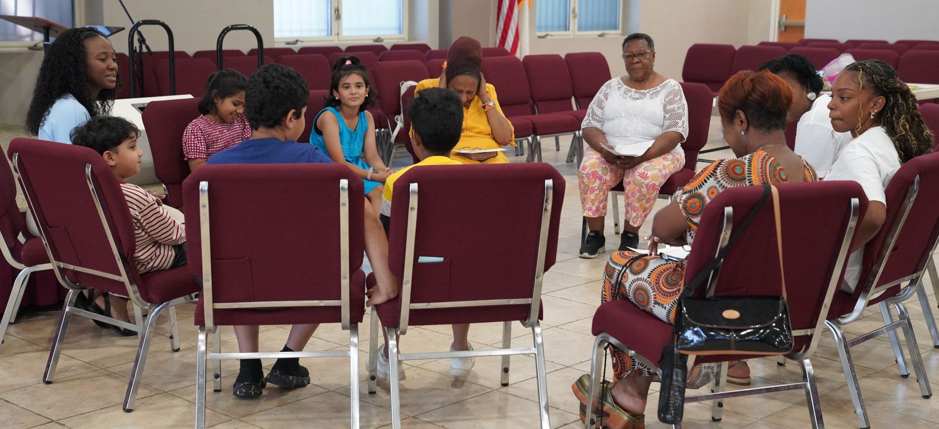 People seated in a circle in a meeting room, engaged in group discussion.