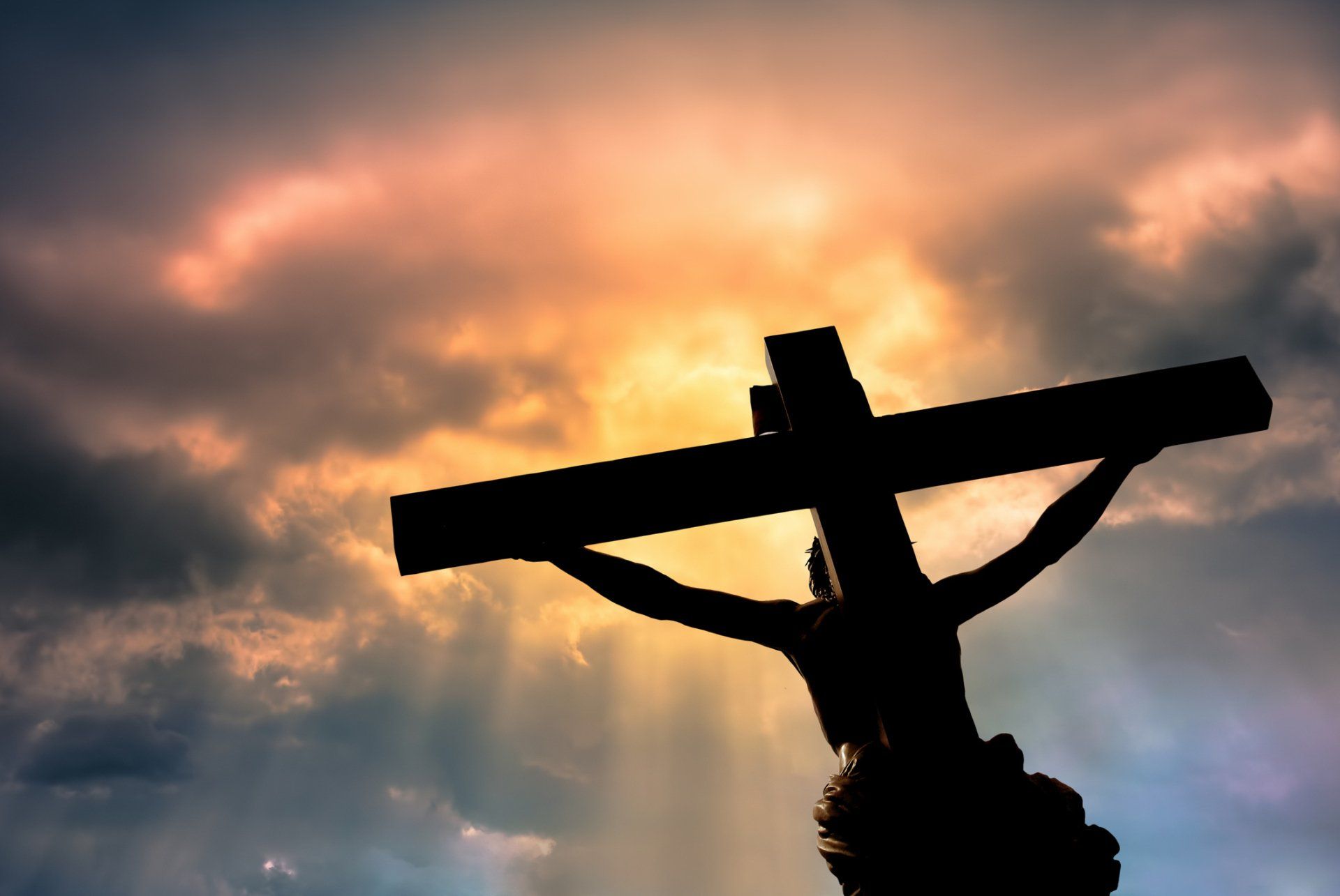 A silhouette of jesus on the cross with a cloudy sky in the background.