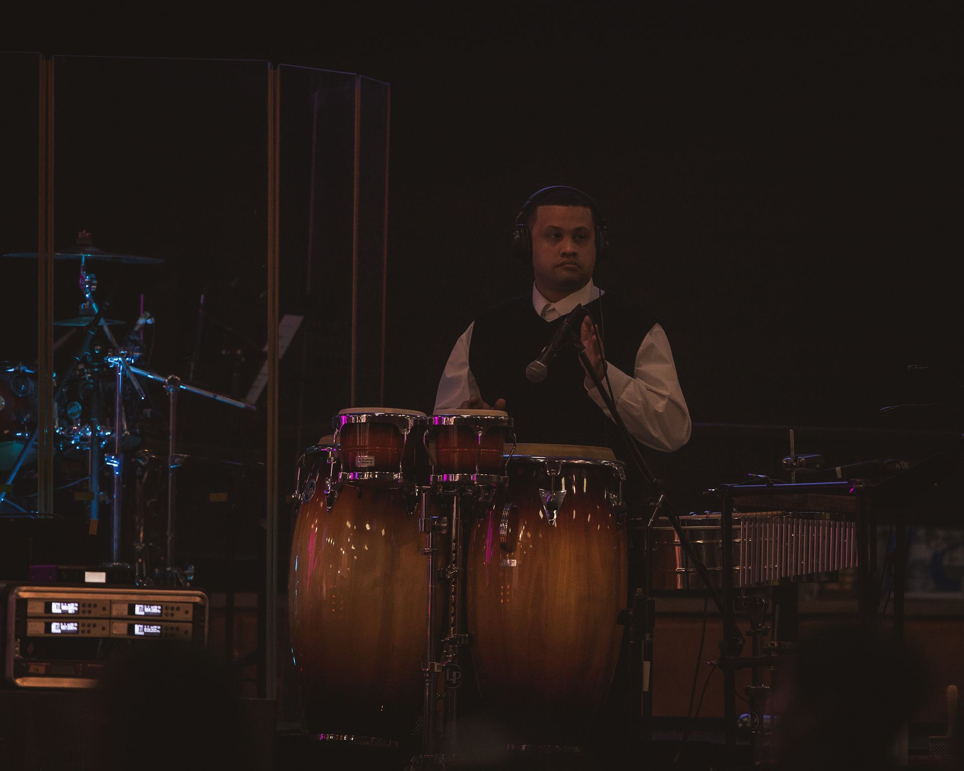 A man is playing drums on a stage in a dark room.