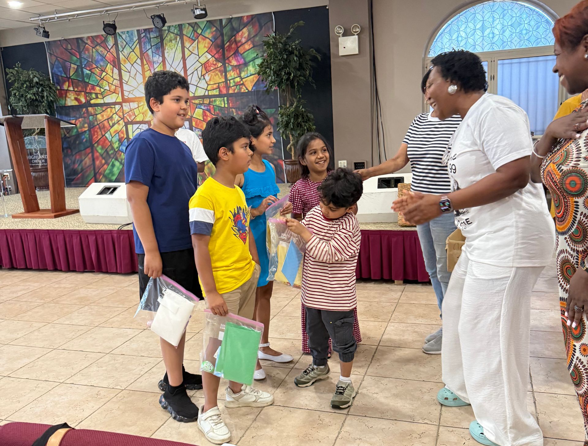 Children and an adult chatting in a hall with a colorful mural backdrop