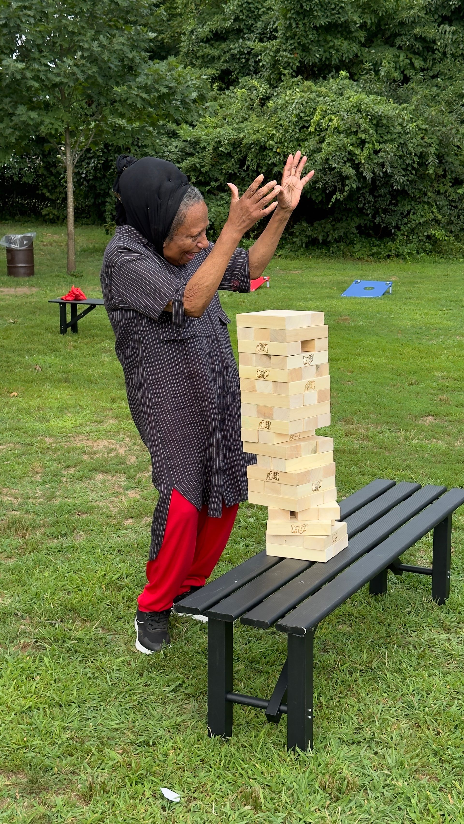 A woman is standing on a bench next to a stack of wooden blocks.