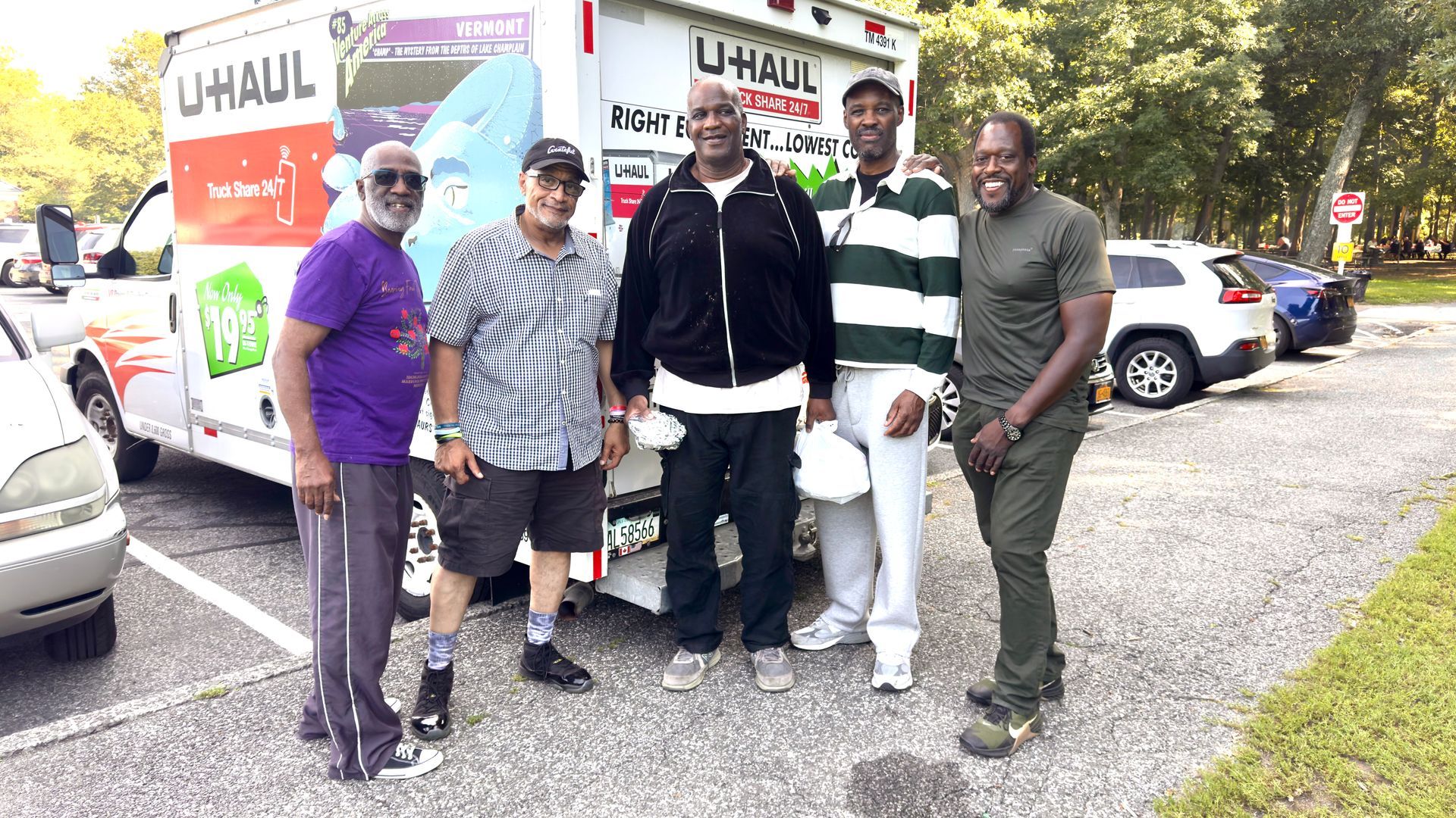 Five people standing beside a U-Haul truck in a parking lot, posing outdoors.