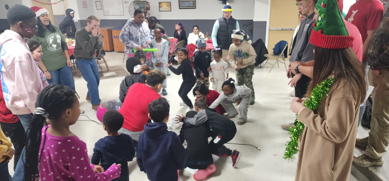 Children and adults gathered in a gym watching a holiday dance performance with festive decorations. Christmas Toy Drive 2025