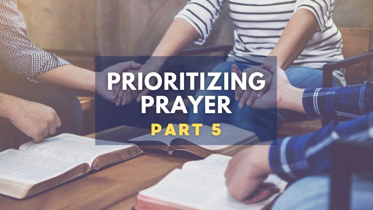 A group of people are sitting around a table holding hands and praying.