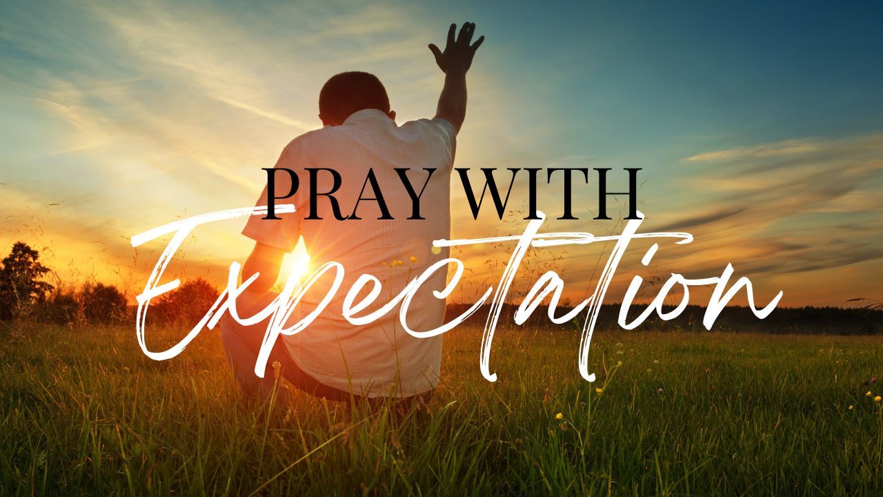 A man is kneeling down in a field with his hands in the air.
