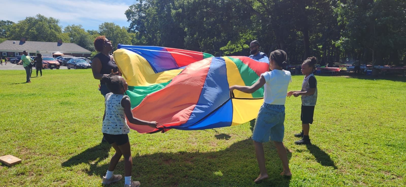 Children holding a colorful parachute on a sunny grassy field outdoors