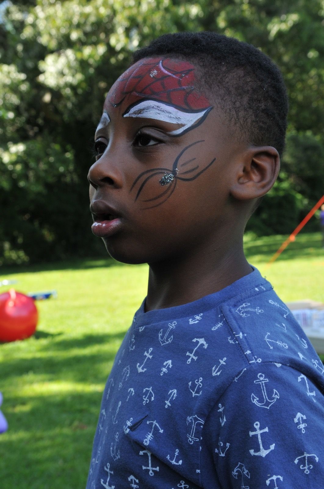 Child with face paint standing outdoors on a grassy lawn.
