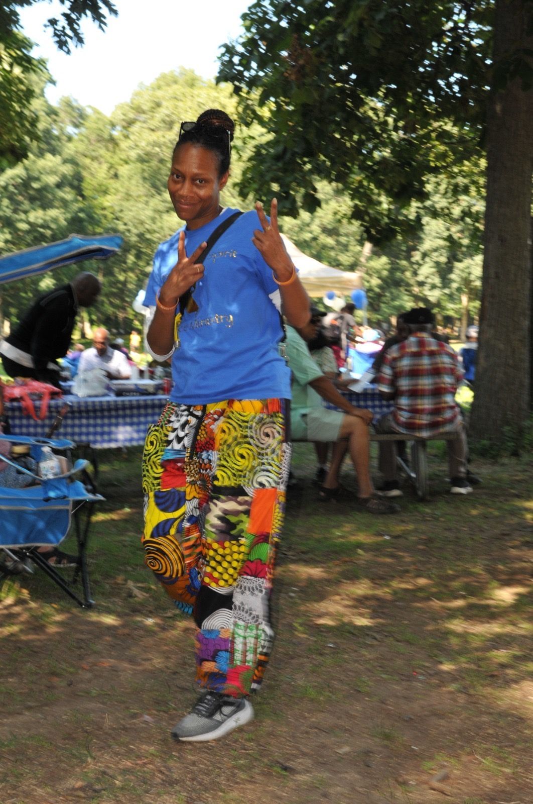 Woman in bright blue shirt and patterned pants posing outdoors at a park picnic.