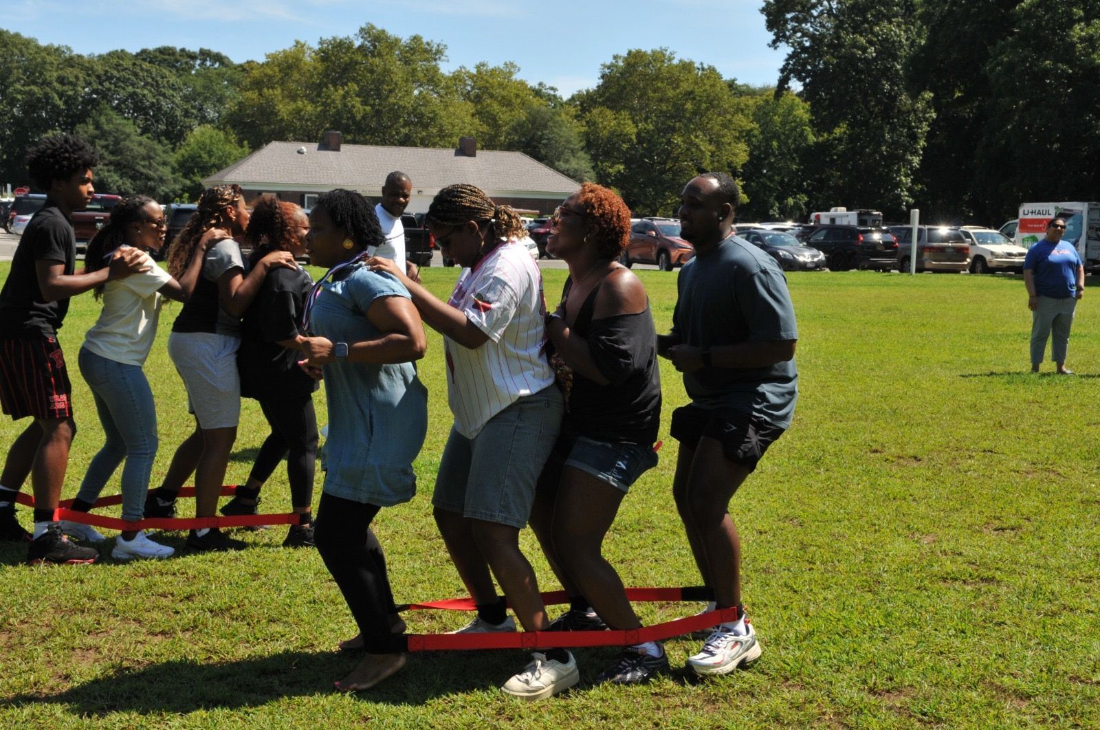People linked by red bands race across a grassy field during an outdoor team activity.