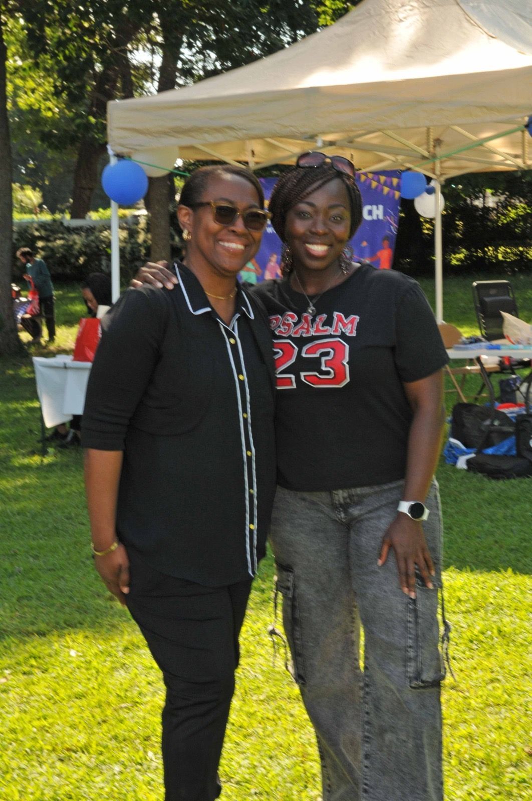 Two people posing together on a sunny lawn in front of a white canopy tent.