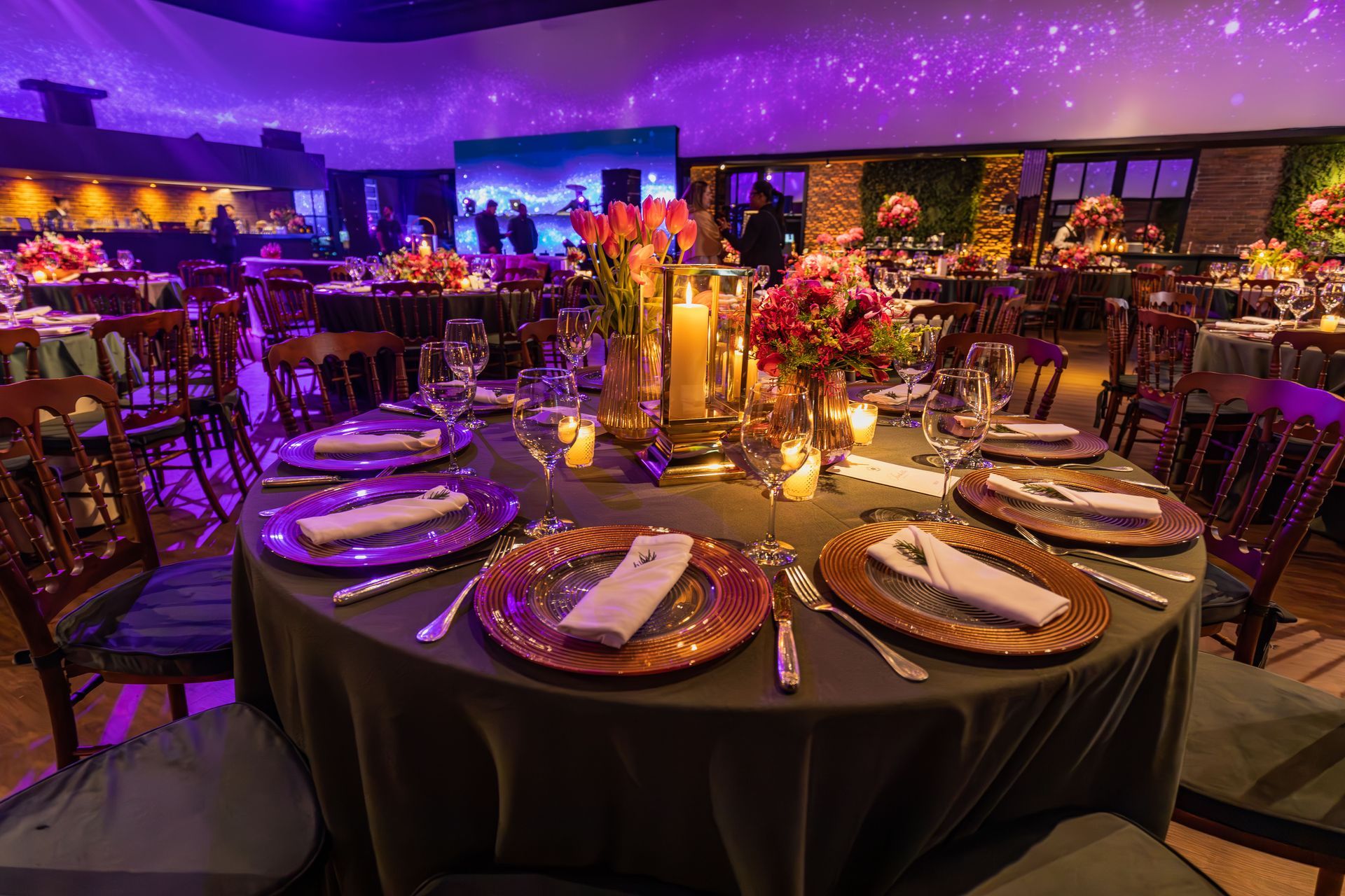 Elegant banquet table set with candles and flowers in a purple-lit event hall