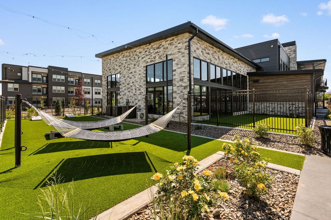 Lawn with hammocks, small building with large windows and brick facade, apartment buildings in background.