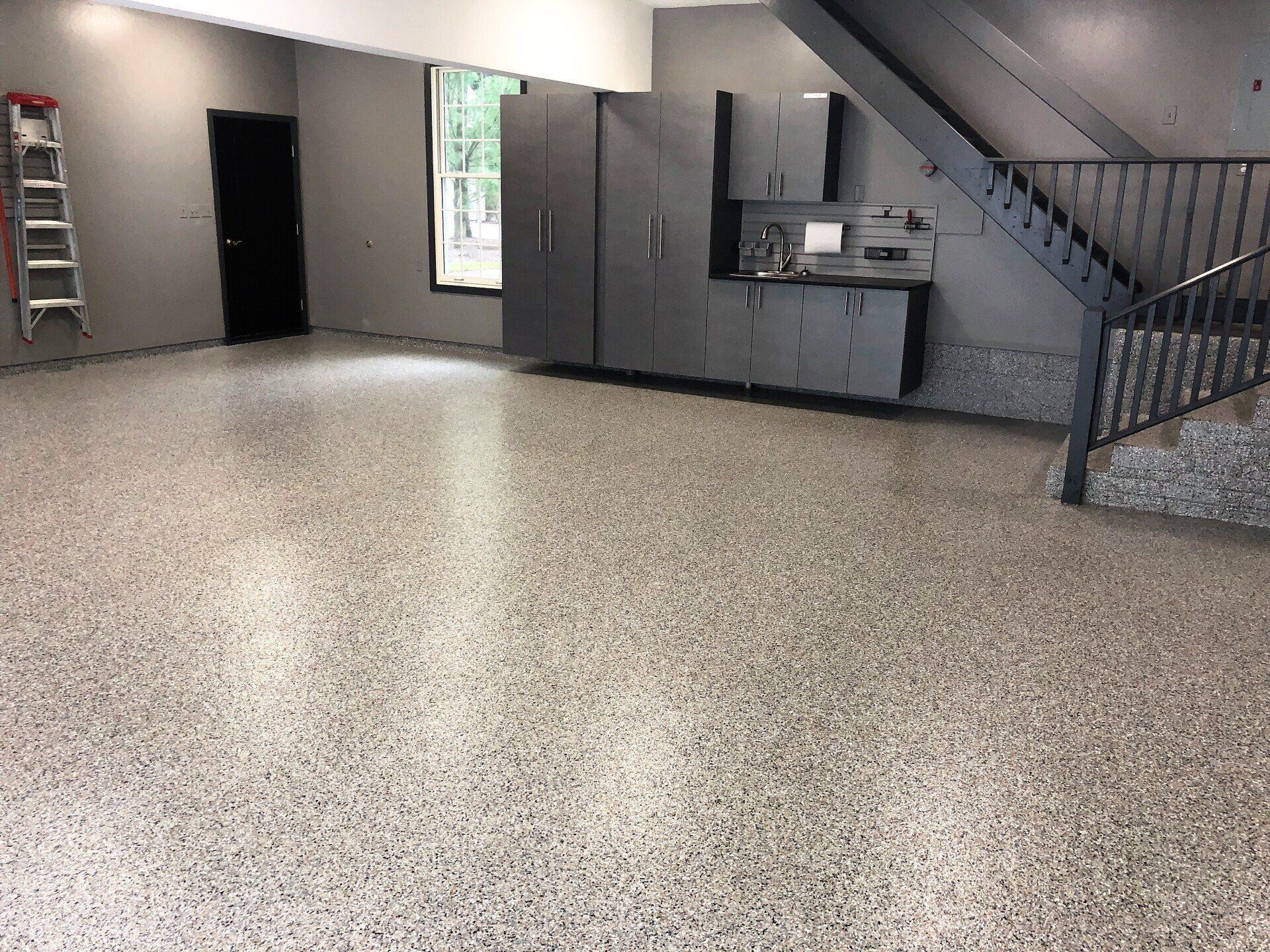 Dark gray cabinets under a staircase in a garage with a flake floor