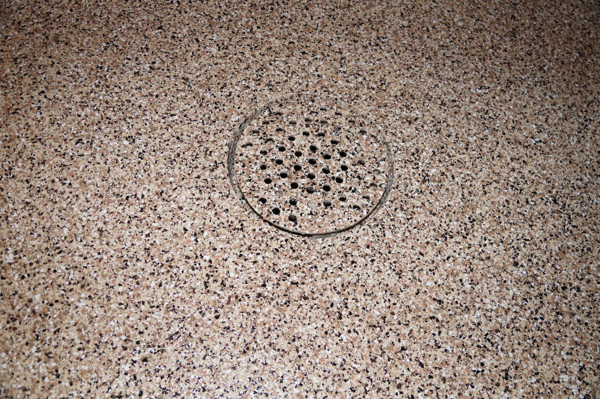 Close-up of a brass floor drain surrounded by tan and black decorative flake polyaspartic coating in