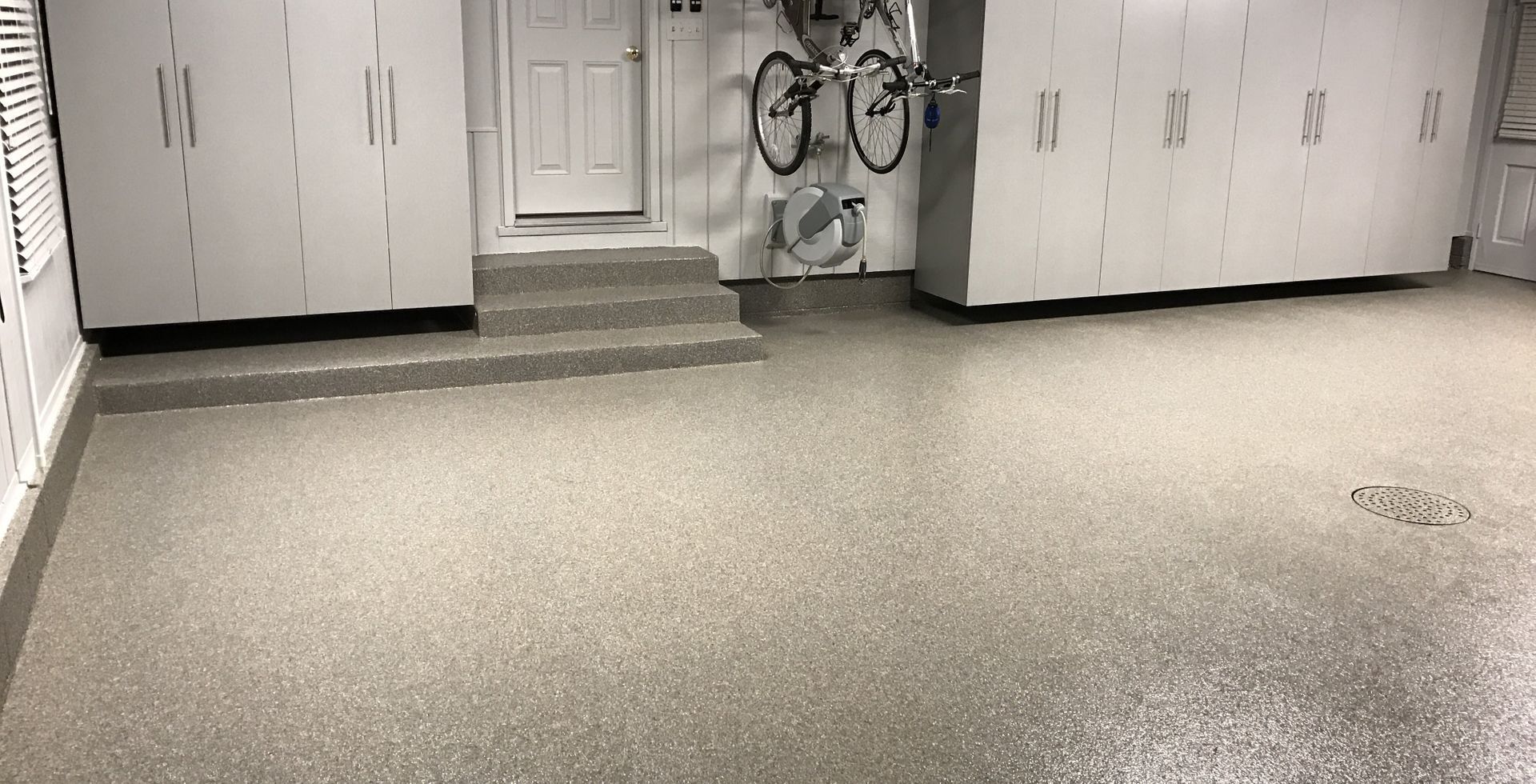 White garage cabinets and bikes on a slatwall over a tan flake floor