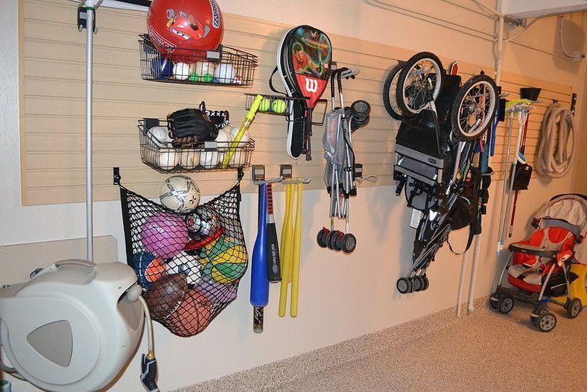 Garage slatwall holding bikes, a stroller, sports balls in a net, and a hose reel