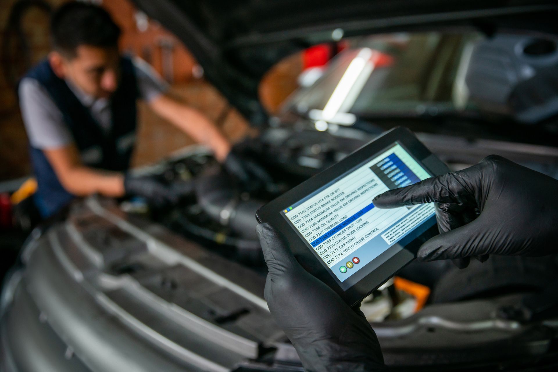 A person wearing black gloves is holding a tablet in front of a car.