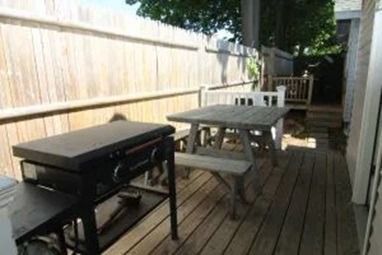 Griddle and picnic table on wooden deck, next to a wooden fence.