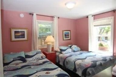 Pink-walled bedroom with two beds, two windows, and a nightstand.