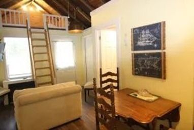 Cozy interior: loft bed with ladder, small sofa, dining table with chairs, two framed chalkboards.