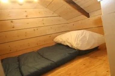 Sleeping bag and pillow in a small, wood-paneled attic space.